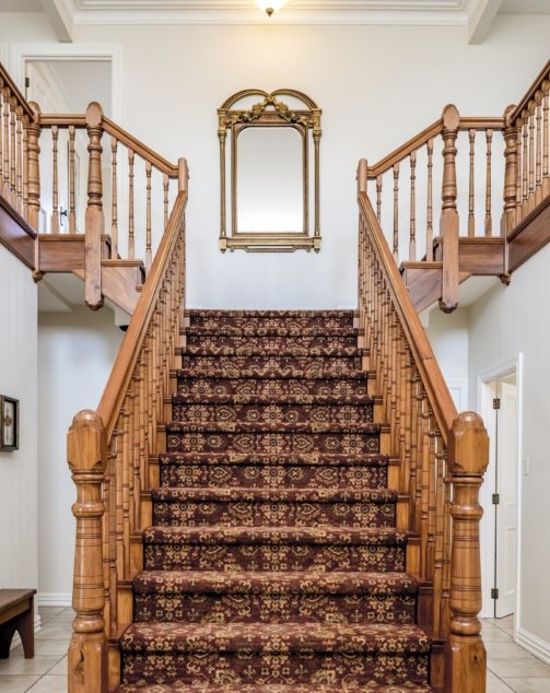 A big wooden staircase with a vintage carpet inside an apartment with white walls