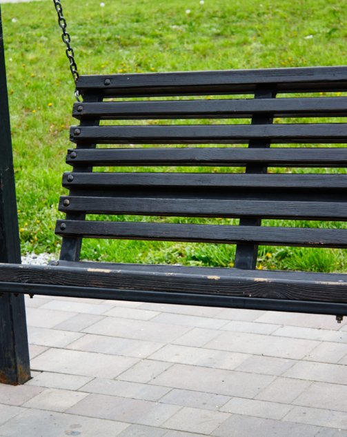 Old black wooden bench on chains in park against backdrop of green lawn. Rest in park. Vacation with children.